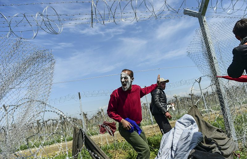 Un hombre llama a otros refugiados para cruzar la valla en la frontera entre Idomeni y Macedonia