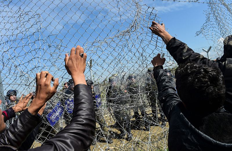 Los refugiados y migrantes intentan tirar una valla fronteriza durante los enfrentamientos con la guardia de Macedonia