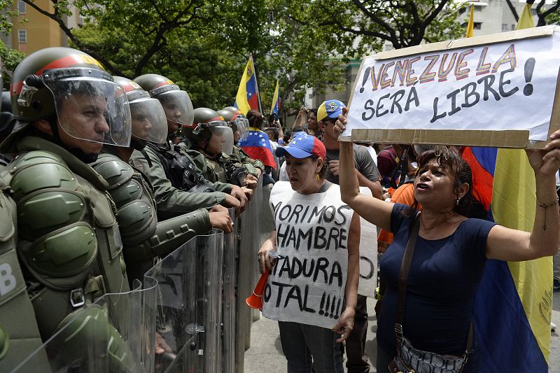 Dos mujeres portando sendas pancartas que rezan "Venezuela será libre" y "Morimos de hambre. Dictadura total".