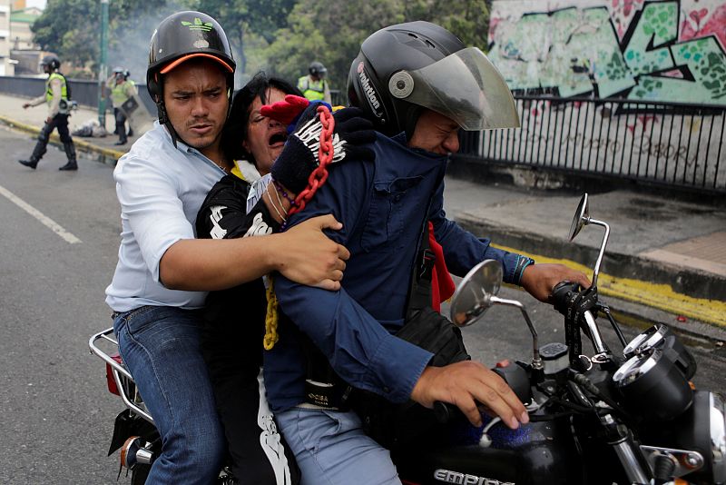 Opositores afectados por los gases lacrimógenos se alejan del lugar en moto