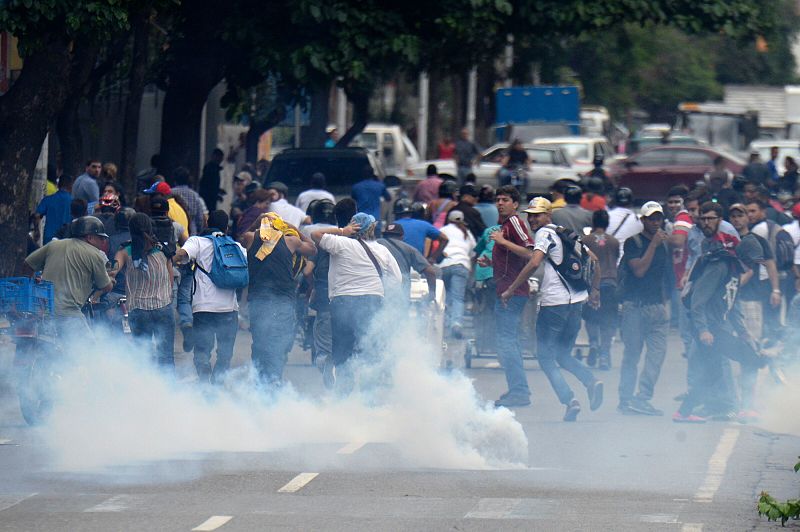 Gente corre por una calle de Caracas después de que la Policía disparara gases lacrimógenos para disolver una manifestación convocada en contra de Nicolás Maduro