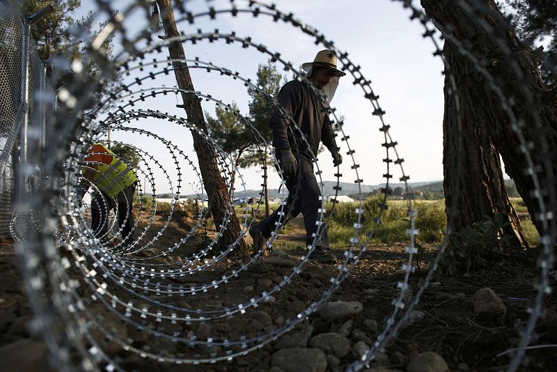 Workers build a barbed wire fence parallel the railway tracks at a makeshift camp near the village of Idomeni