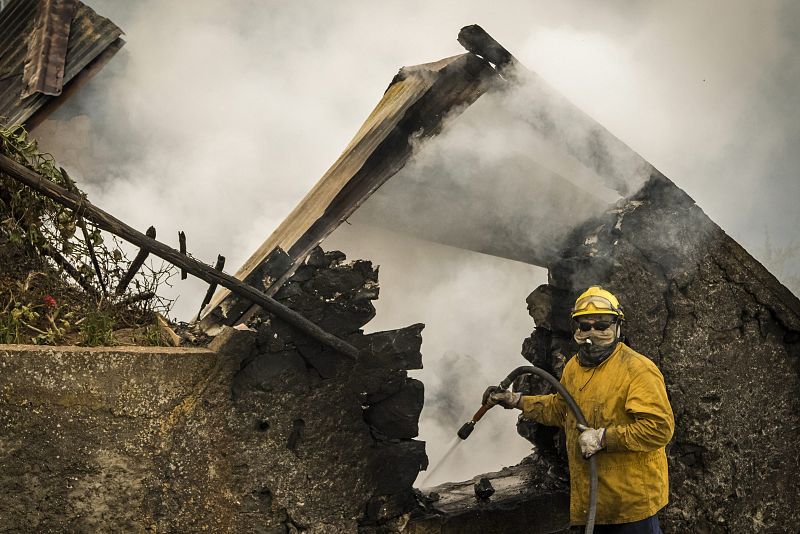 Un hombre del cuerpo de bomberos refresca los restos calcinados de una casa