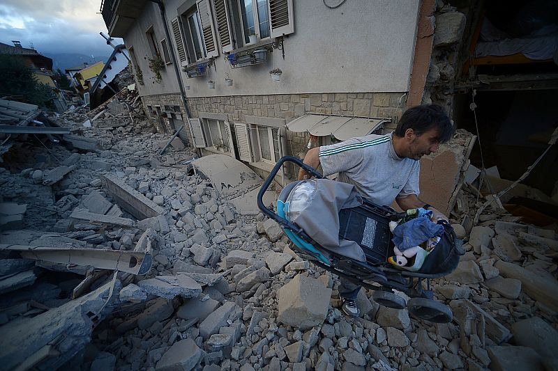 Un hombre carga consigo un carrito de bebé entre los escombros de las casas derruidas.