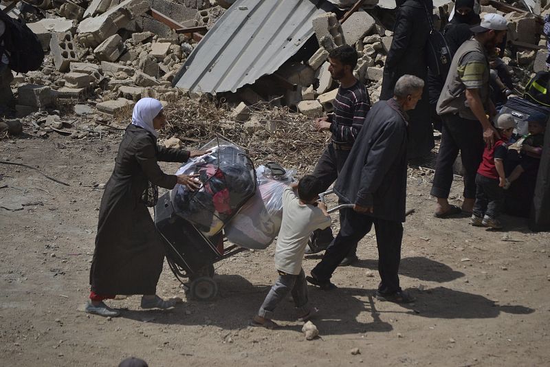 Varias familias portan sus pertenencias mientras abandonan Daraya