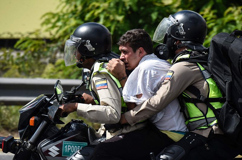 Dos policías en motocicleta custodian a un opositor arrestado en la manifestación en Caracas