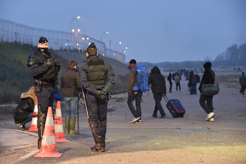 Migrantes pasan frente a los policías desplegados en el campamento de "La Jungla" de Calais