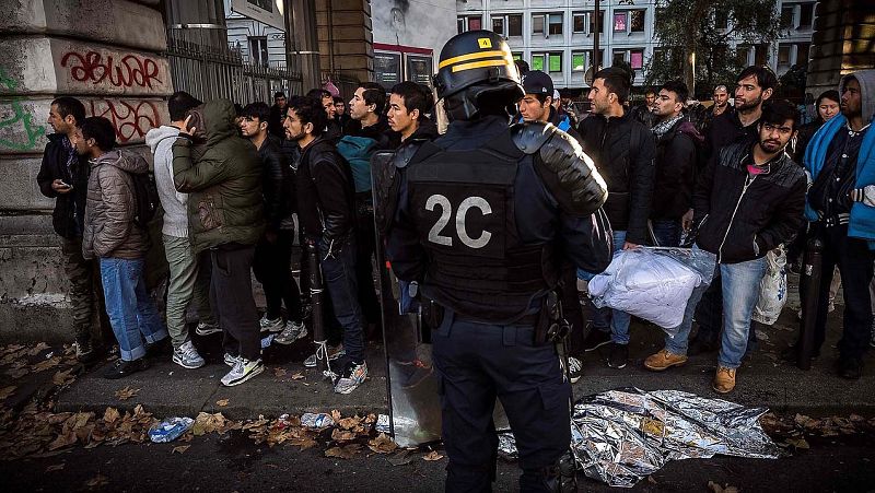 Policías antidisturbios ante una fila de migrantes cerca de las estaciones de metro de Jaures y Estalingrado, en París.