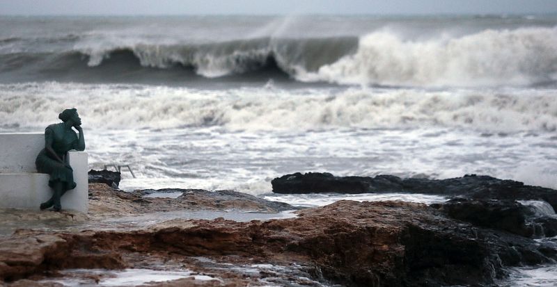 Las olas rompen contra las rocas tras la escultura de la bella Lola, en el paseo marítimo de Torrevieja (Alicante).