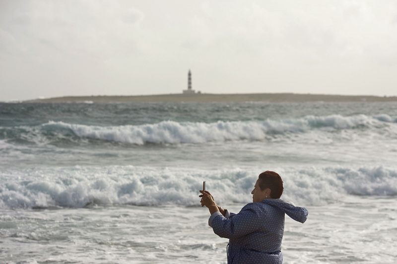 Una mujer hace una fotografía en la playa de Punta Prima en el municipio de San Lluís, afectada por el temporal de lluvia y viento.