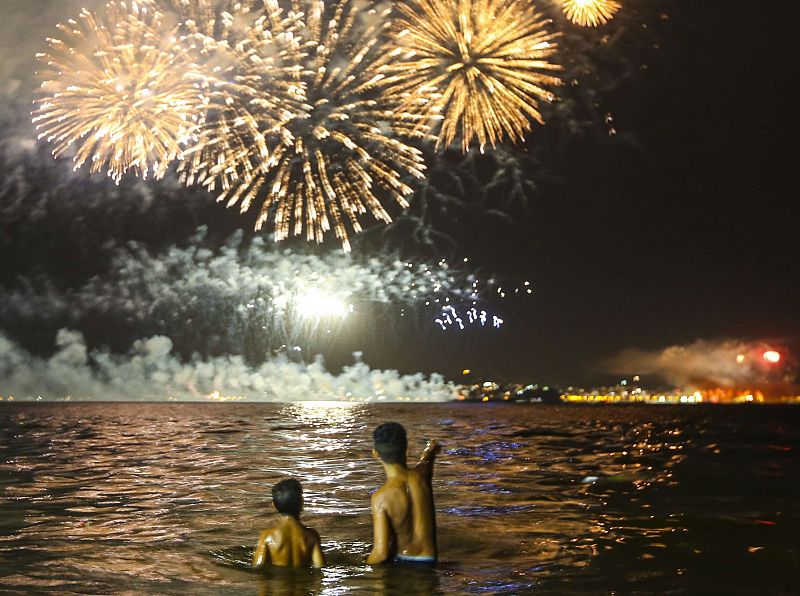 Dos chicos presencian desde el agua los fuegos artificiales en la playa de Flamengo en Río de Janeiro, Brasil
