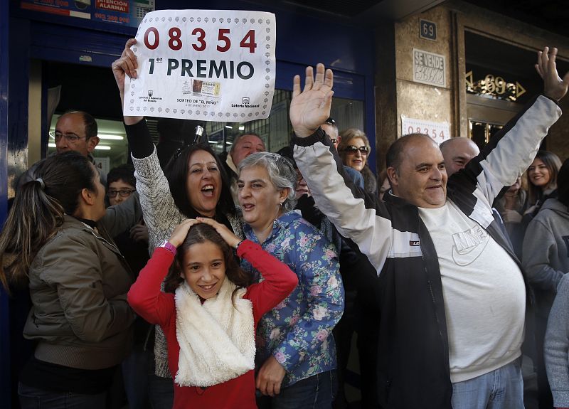 Agraciados con el primer premio del sorteo de El Niño, dotado con 2.000.000 de euros a la serie, lo celebran con el número en la mano, en las puertas de la administración número 3 de Torrent (Valencia)