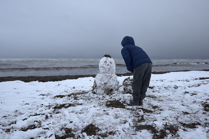 Un niño juega con un muñeco de nieve en la playa de Les Marines, en Denia, completamente nevada desde primeras horas de la mañana.