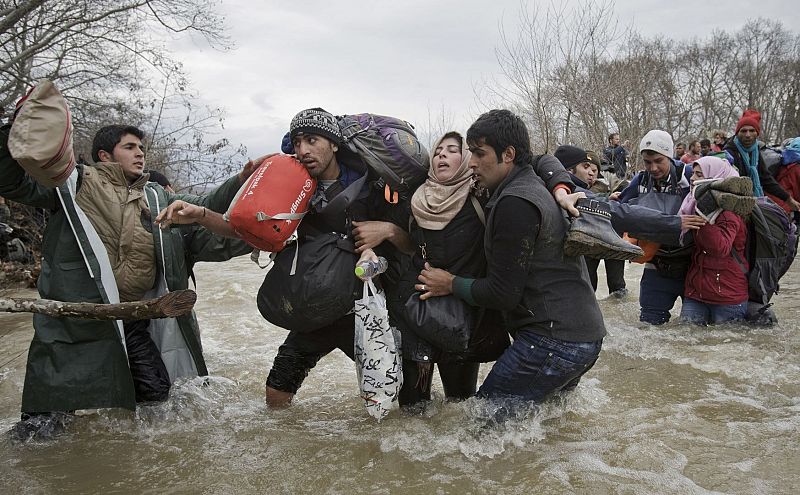 La imagen muestra el momento en el que dos refugiados ayudan a una mujer a cruzar un río en su ruta a Macedonia el 14 de marzo de 2016. Centenares de refugiados abandonaron ese mismo día el campamento en el que permanecían instalados en la frontera e