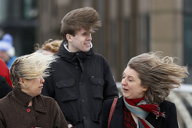 Pedestrians have their hair blown as they walk during strong winds in London