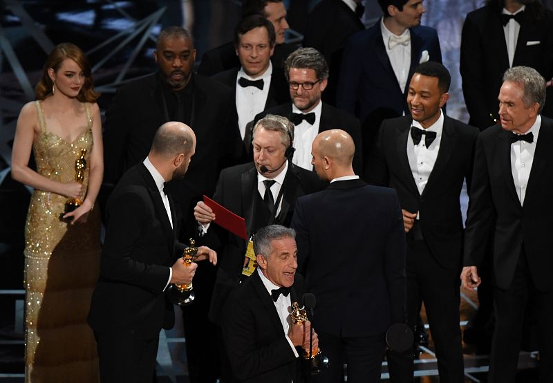 Jordan Horowitz habla con uno de los productores de la gala mientras el resto del equipo celebra y agradece el Oscar a la mejor película