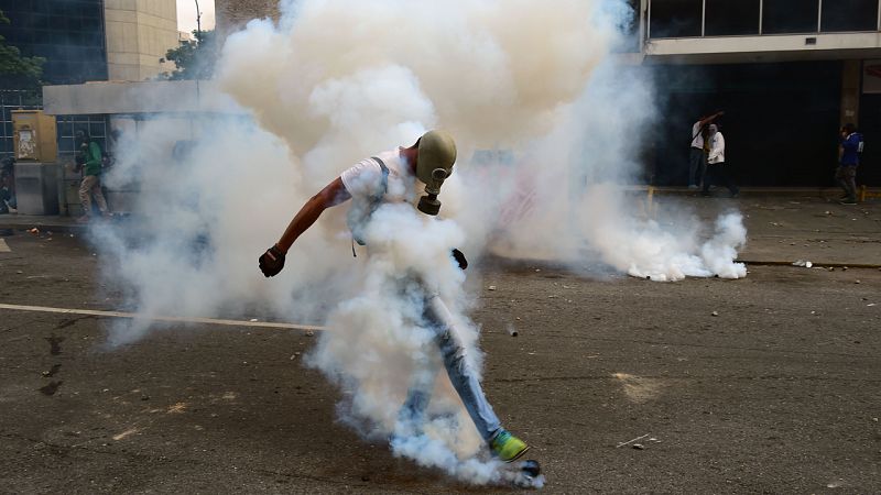 Un manifestante envuelto en gases lacrimógenos se enfrenta a la policía venezolana