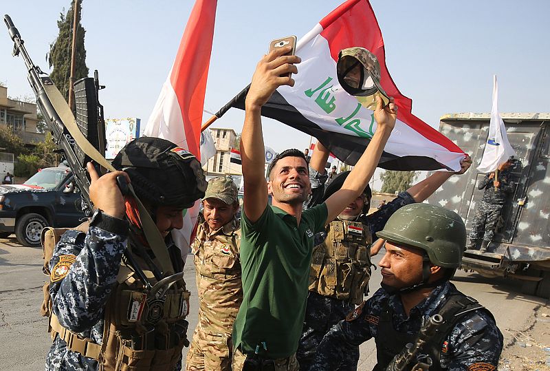 Un civil tomando una foto con su móvil junto a miembros de la policía federal que celebran la victoria en la Ciudad Vieja de Mosul