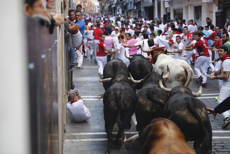 Los toros de la ganadería madrileña de Victoriano del Río llegan a la curva de Mercaderes en el sexto encierro de Sanfermines Muchos corredores han caído y se han quedado en el suelo, como indica el reglamento, para protegerse del paso de los astados