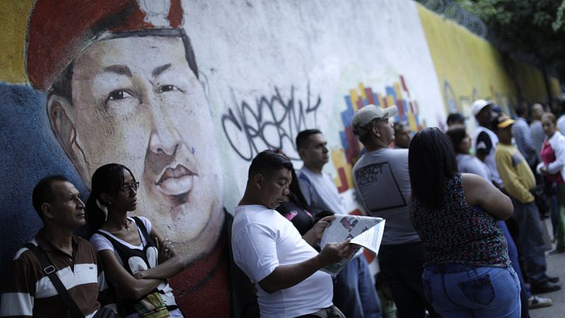 Decenas de venezolanos esperan para votar junto a una imagen del anterior presidente del país, Hugo Chávez.