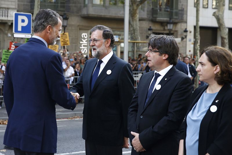 El rey Felipe saluda al presidente del Gobierno, Mariano Rajoy (2i), ante el presidente de la Generalitat, Carles Puigdemont (2d), y la alcaldesa de Barcelona, Ada Colau, durante la manifestación contra los atentados yihadistas en Cataluña.