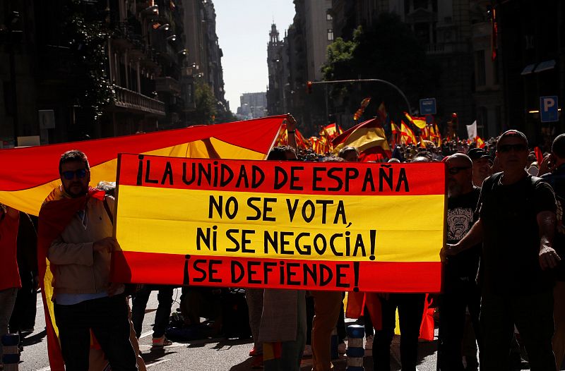 Dos personas sujetan una bandera de España con la siguiente inscripción: "¡La unidad de España no se vota ni se negocia! ¡Se defiende!