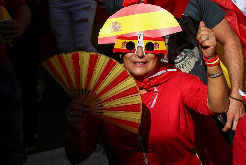 Una mujer con un sobrero y una gafas con los colores de la bandera de España y un abanico con los colores de la bandera de Cataluña