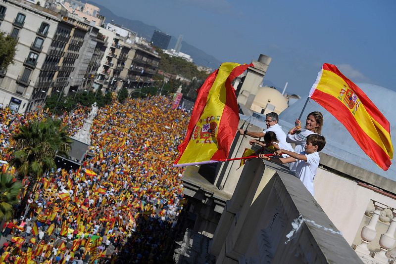 Una familia ondea banderas de España desde una azotea al paso de la manifestación que recorre Barcelona en defensa de la unidad de España