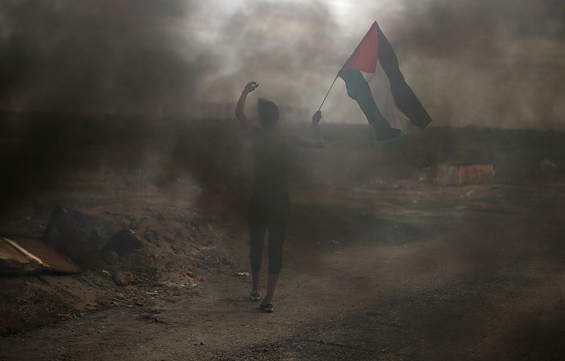 Un palestino sujeta una bandera durante los enfrentamientos con tropas israelíes cerca de la frontera de Gaza con Israel