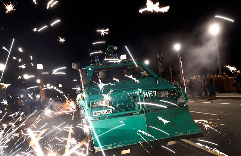 Fireworks explode next to an armored police vehicle closing a bridge over river Main as revellers start to celebrate New Year's eve in Frankfurt