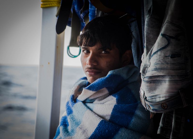 Joven rescatado por OPEN ARMS cubierto con su manta mientras su ropa se seca.