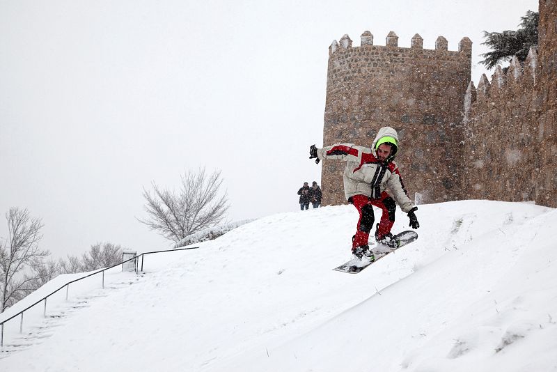 Un hombre se divierte con su tabla de 'snowboard' junto a la muralla de Ávila