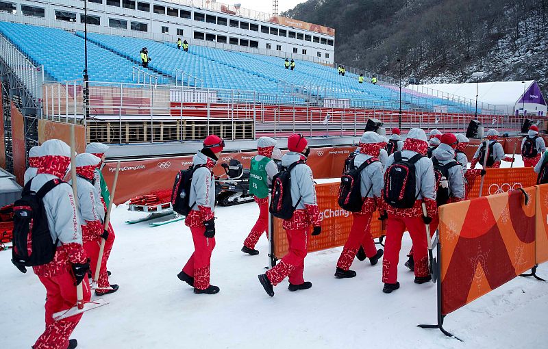 Un grupo de voluntarios abandonan las instalaciones del centro alpino tras la suspensión de la prueba del domingo.