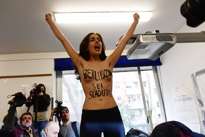 Una mujer protesta en la mesa electoral donde vota Silvio Berlusconi, en Milán, con una frase pintada en su cuerpo que reza: "Berlusconi, has caducado"