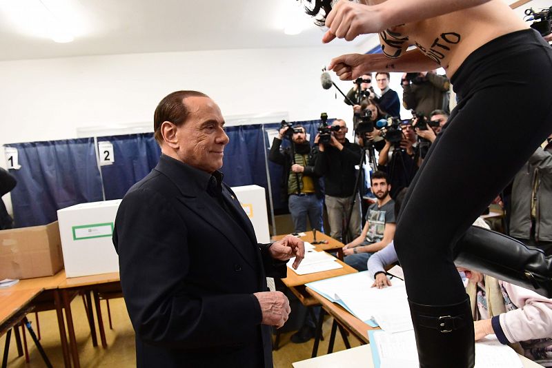 Una mujer en toples salta sobre una mesa delante de Berlusconi en un colegio electoral de Milán