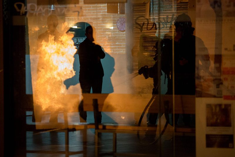 Imagen de varios bomberos en un escaparate mientras trabajan para sofocar los fuegos provocados