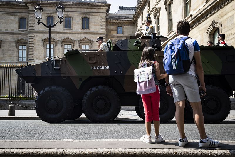 Un padre y su hija observan el paso de un vehículo militar delante del Museo del Louvre
