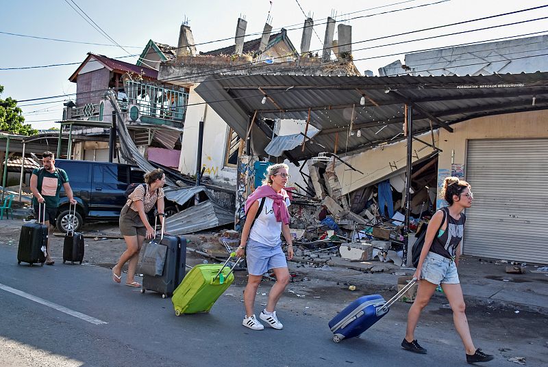 Turistas acarrean sus equipajes junto a edificios dañados por el temblor