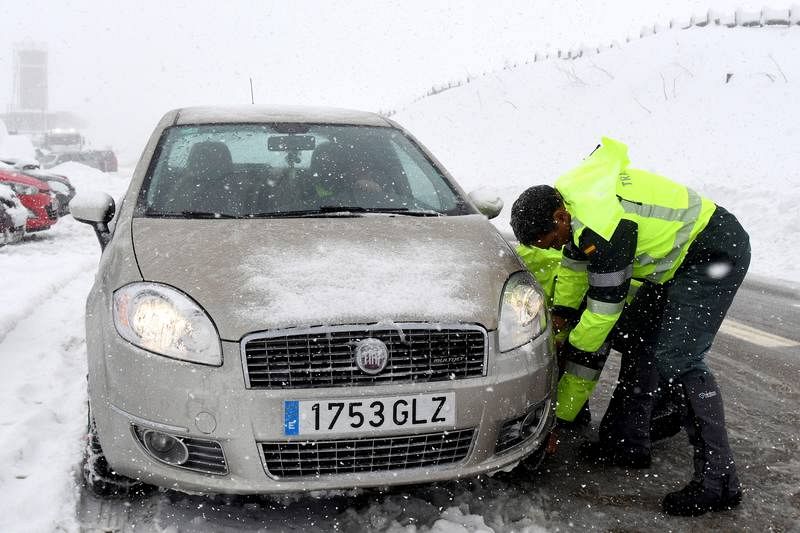 Un miembro de la Guardia Civil ayuda a poner las cadenas a un vehículo en el Puerto de Pajares