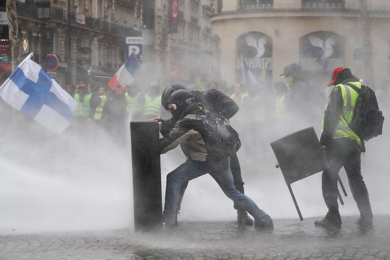 Un grupo de manifesantes se protege de un cañón de agua en los Campos Elíseos