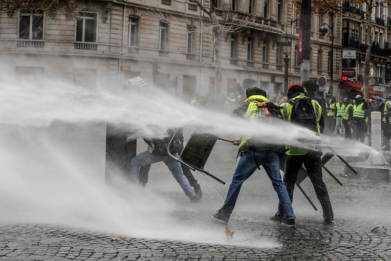 Un grupo de manifestantes se defiende con mobiliario urbano de un cañón de agua usado por la policía