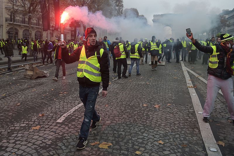 Un manifestante porta una bengala mientras el gas lacrimógeno se adueña de los Campos Elíseos