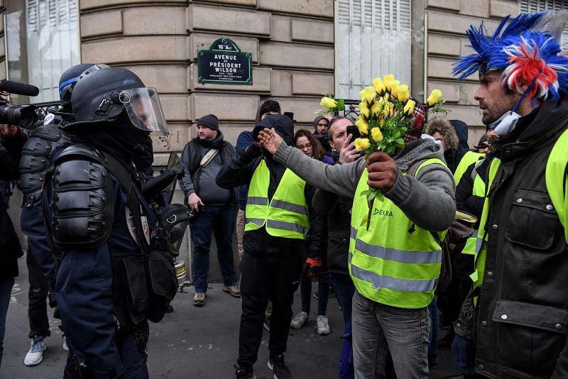 Un manifestante con un ramo de rosas amarillas habla con un policía