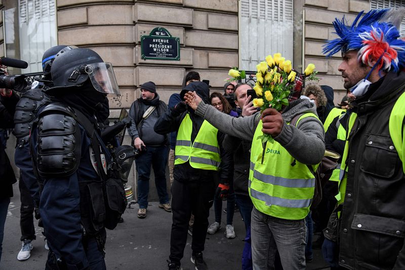 Un manifestante con un ramo de rosas amarillas habla con un policía