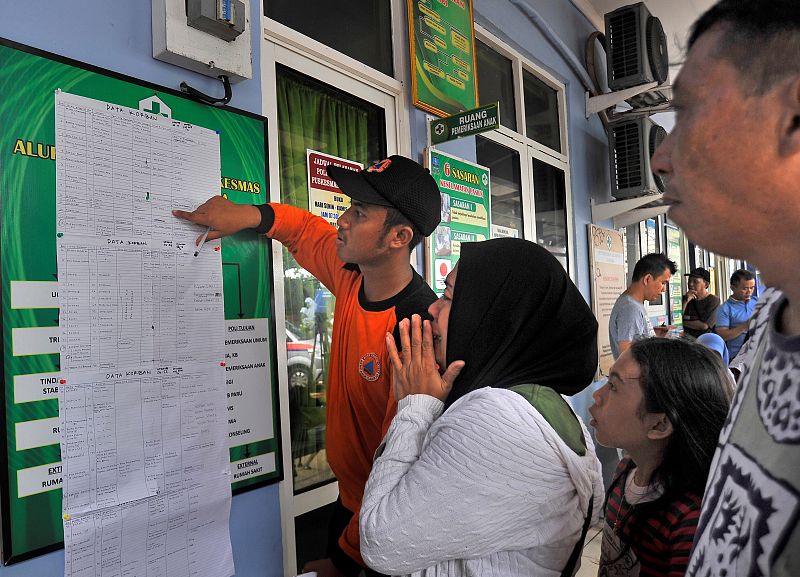 Un grupo de personas lee un listado de víctimas mortales del tsunami