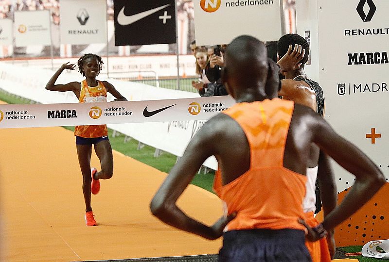 La keniana Brigid Kosgei (i), entra vencedora de la San Silvestre Vallecana, ante la mirada de los ganadores de la prueba masculina.