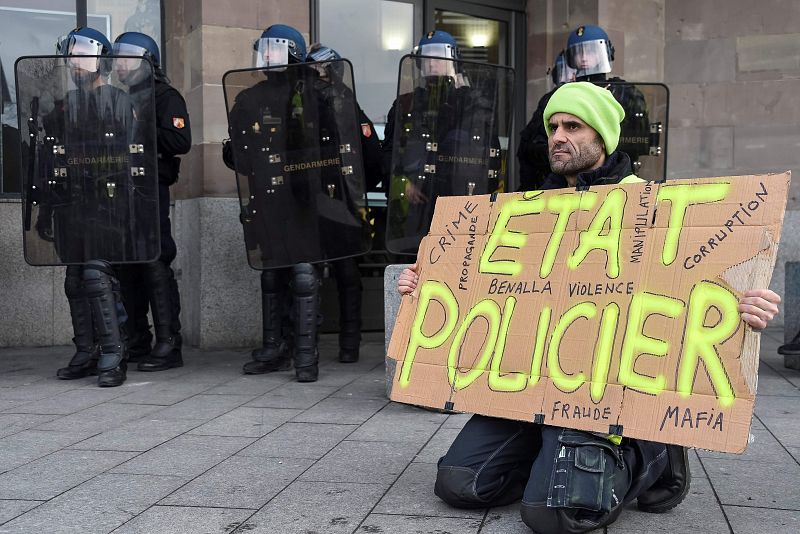 Un hombre sujeta una pancarta que reza "Estado policial" se arrodilla delante de varios miembros de la policía antidisturbios en Mulhouse