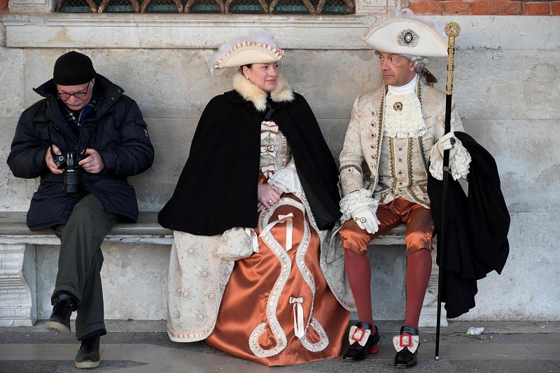 Un turista comprueba su cámara sentado junto a una pareja vestida con trajes de época