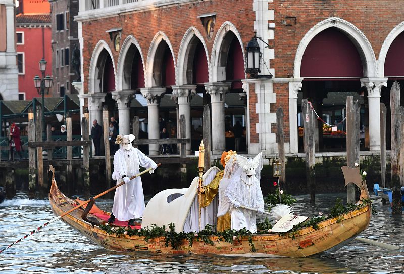 Tres personas ataviadas con los trajes tradicionales del carnaval veneciano navegan el Gran Canal en una góndola