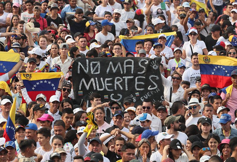 Asistentes al Venezuela Aid Live portan pancartas con mensajes de rechazo al presidente Nicolás Maduro, que al otro lado del puente celebra su concierto "por la paz".